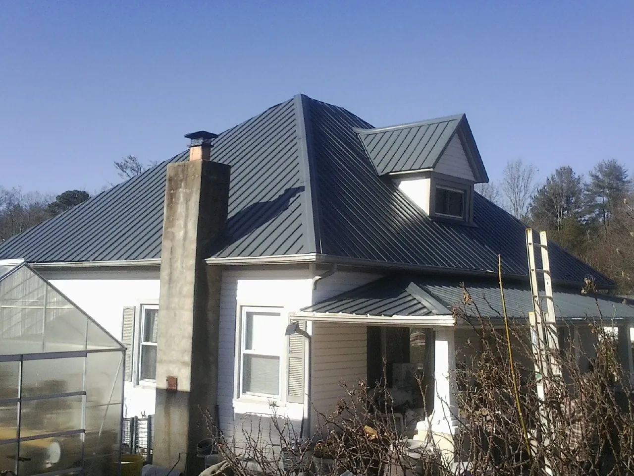 Dark blue standing seam metal roof on a white farmhouse with dormer — Slate & Tile Roof Repair by Roofing Brothers in Machesney Park