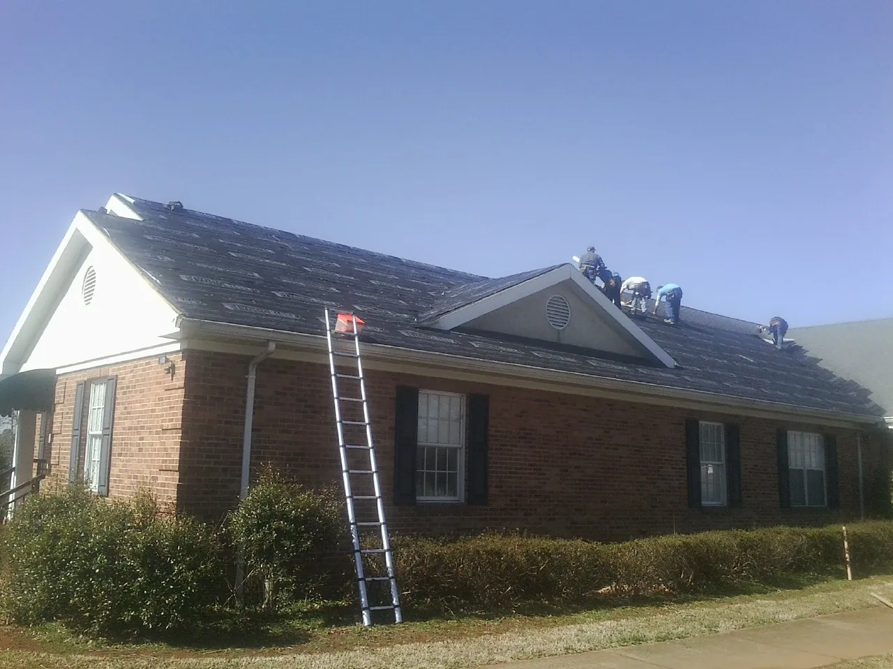 Crew tearing shingles off a brick ranch roof with a ladder set — Metal Roof Repair work by our crew in Machesney Park