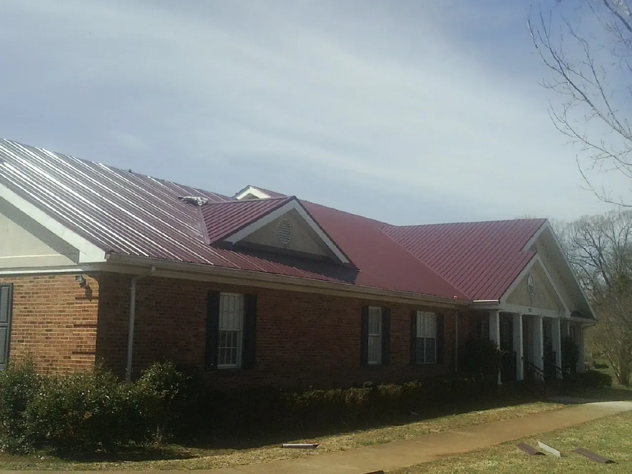 Red metal roof with gabled entries on a long brick building, from a Hail Damage Roof Repair job in Machesney Park
