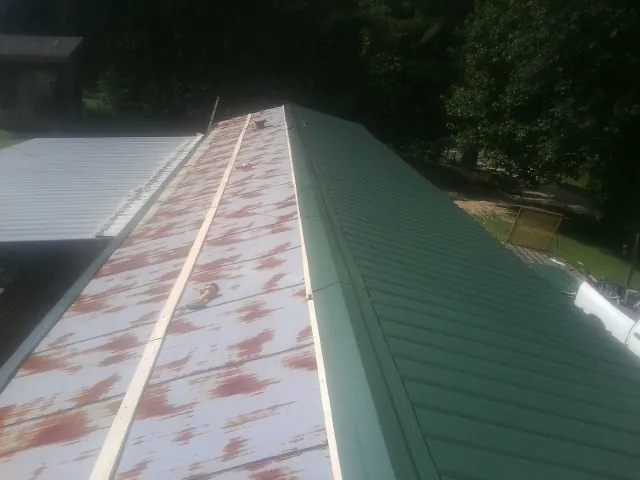 Old rusted panels beside newly installed green metal roofing — Wind Damage Roof Repair by Roofing Brothers in Machesney Park