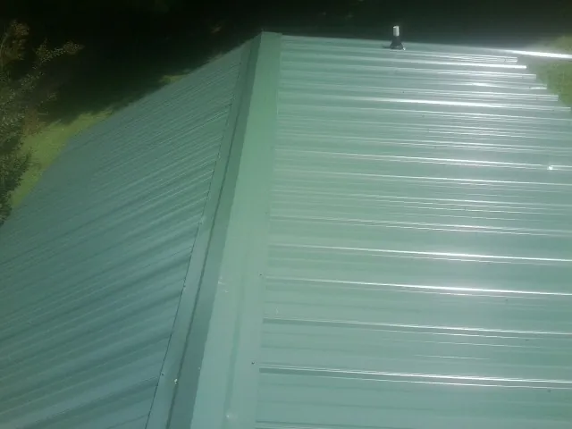 New green metal panels meeting at the ridge of a roof — Flat Roof Repair work by our crew in Machesney Park