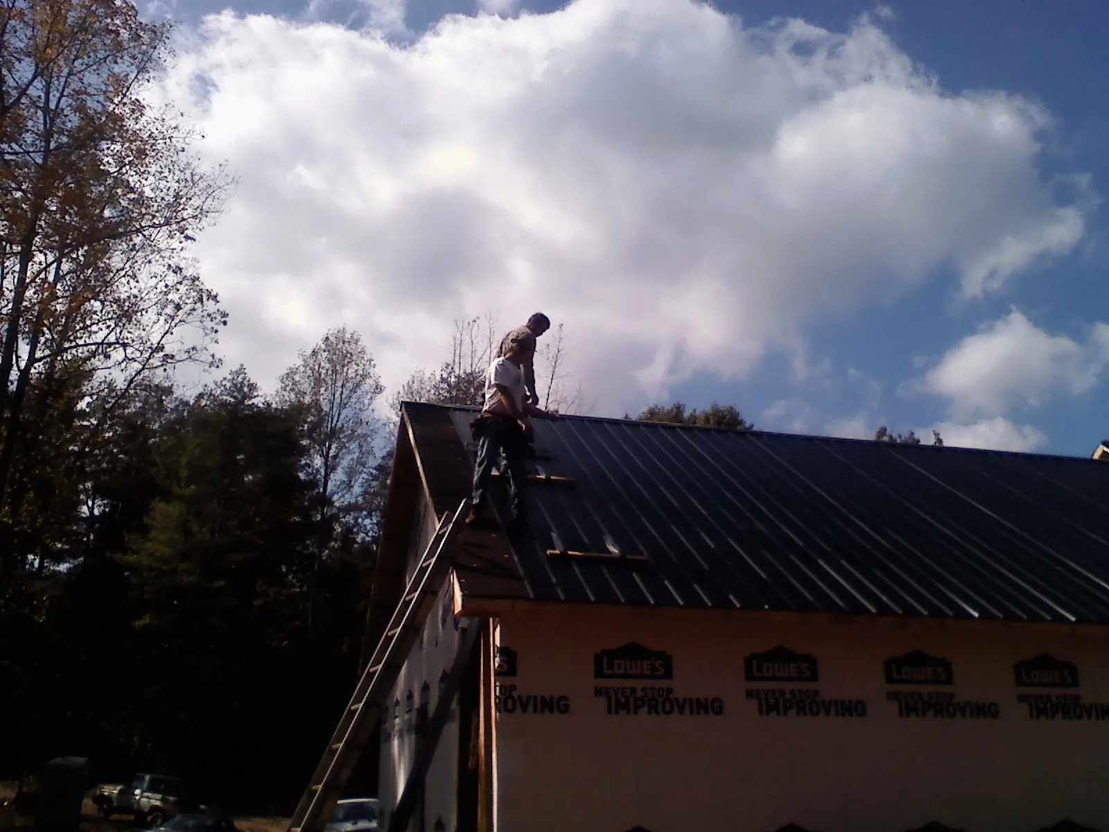 Roofer fastening dark metal panels high against a cloudy sky, from a Roof Inspection job in Machesney Park