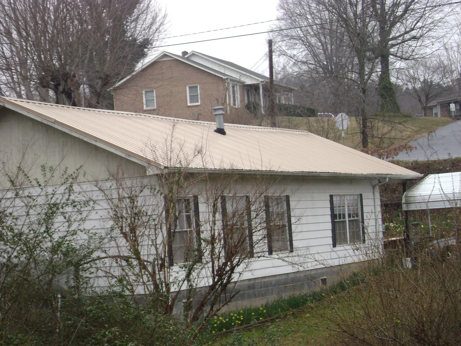 Tan metal roof on a white sided house set into a hillside — Commercial Roofing by Roofing Brothers in Machesney Park