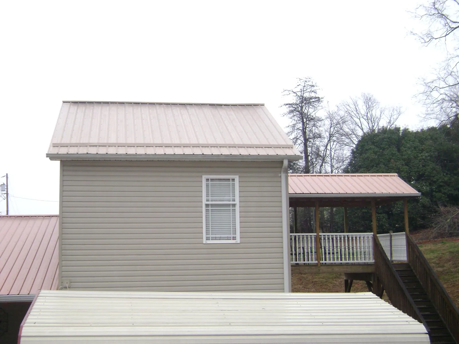 Tan metal roofs on a two story addition and attached porch, from a Roof Replacement job in Machesney Park